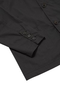 Camicia nera con bottoni, caratterizzata da una texture liscia e opaca; presenta un colletto dritto, maniche lunghe e quattro bottoni scuri ai polsini.