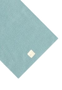 Campione di tessuto di colore azzurro chiaro con una piccola etichetta bianca cucita vicino a un angolo, su uno sfondo bianco.
