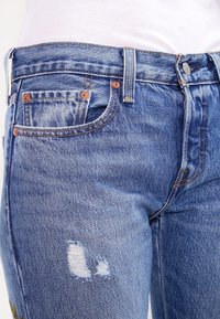 Ljusblå denimjeans med slim fit, kopparfästen, synlig fickdesign och slitningar nära knät.