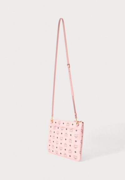 Sac bandoulière MCM rose avec une sangle réglable et un motif répété de logo marron sur la surface, sur un fond uni.