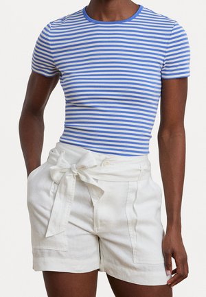 Persona vistiendo una camisa de manga corta a rayas azules y blancas metida en shorts blancos de talle alto con un cinturón atado y bolsillos delanteros.