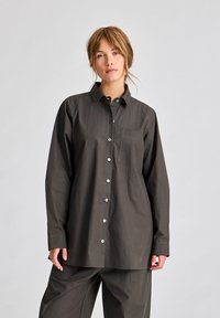 Camicia a maniche lunghe grigio scuro con colletto, taschino frontale e bottoni metallici. Realizzata in tessuto liscio, presenta una vestibilità comoda.