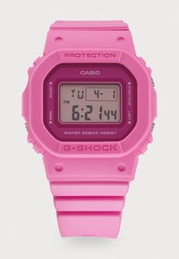 Montre numérique rose avec un cadran carré, un bracelet en caoutchouc et des boutons sur le côté. Résistante à l'eau, elle affiche l'heure et la date.