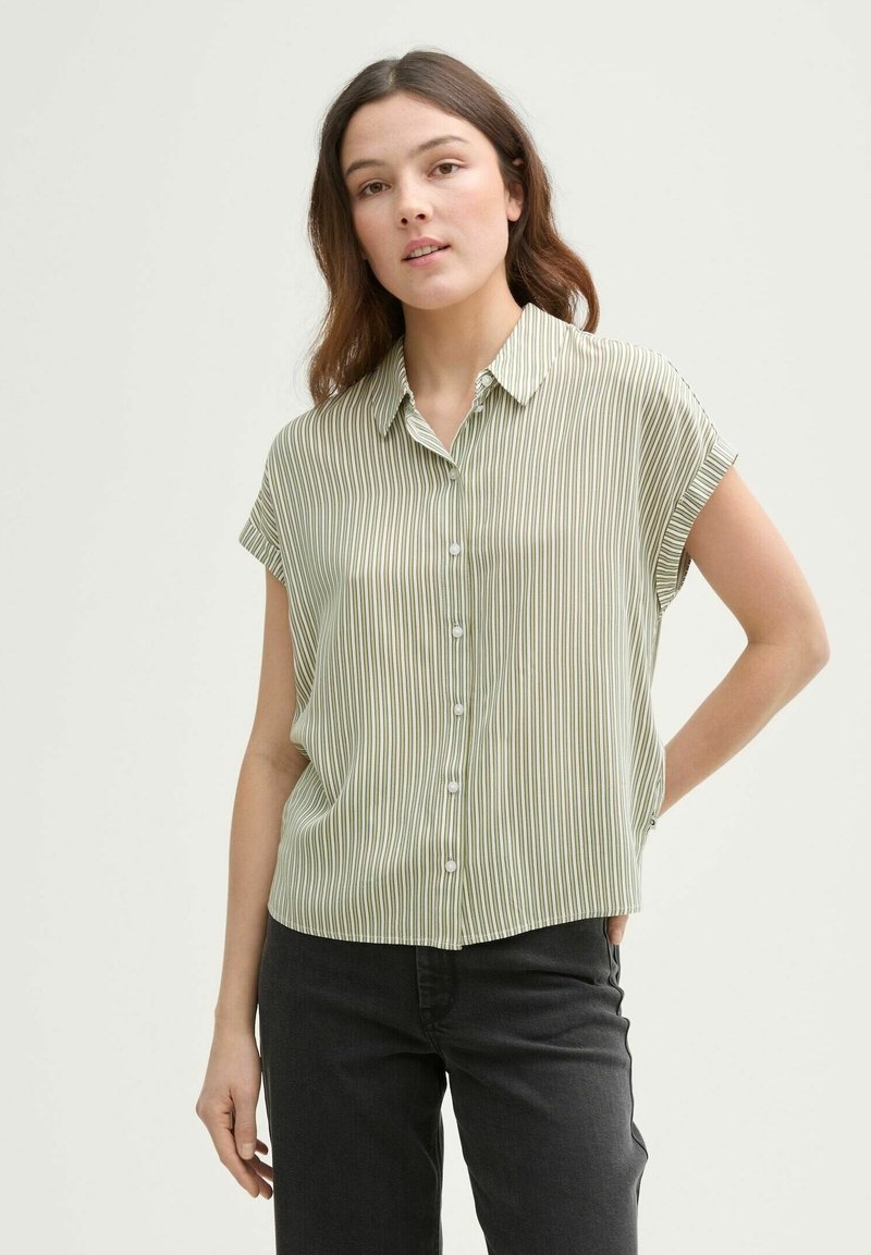 Blusa a maniche corte a righe verdi con abbottonatura frontale e un tessuto morbido e leggero. Indossata con pantaloni scuri, caratterizzati da una vestibilità comoda.