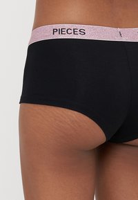 Černé spodní prádlo s jemným povrchem, které má lesklý růžový pás s nápisem "PIECES", nabízí těsný střih v stylu slipů.