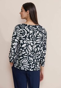 Maglietta a maniche lunghe di colore blu navy con motivi floreali bianchi e spirali, dotata di scollatura rotonda e vestibilità comoda. Tessuto liscio con una sottile texture.