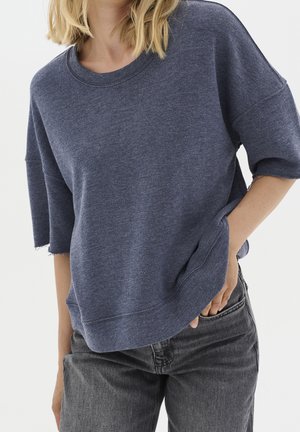 Navyblaues, übergroßes Sweatshirt aus einem weichen, strukturierten Stoff mit überschnittenen Schultern und fransigen Kanten, kombiniert mit dunkelgrauen Jeans.