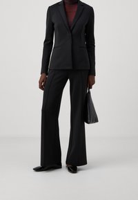Svart skräddarsydd kostym med en strukturerad kavaj och vida byxor. Slät tyg, minimalistisk design, kombinerad med en svart handväska och stiliga skor.