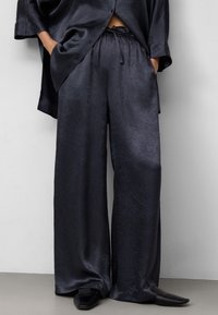 Locker sitzendes, dunkelgraues Satin-Oberteil und weit geschnittene Hose mit subtiler Textur. Die Hose hat einen elastischen Bund und eine Kordelzugdetails.