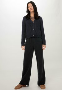 Marineblauwe ribgebreide cardigan met V-hals, drie knopen en cropped ontwerp, gecombineerd met hoge zwarte wijde broek en loafers.