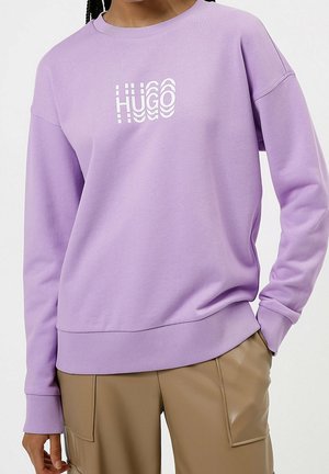 Lila sweatshirt med ribbade muddar och fåll, med en vit logotryck. Tyget ser mjukt ut med en avslappnad passform.