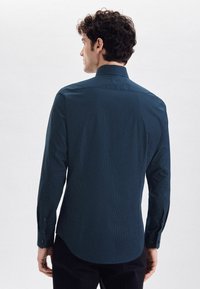 Ciemnozielona koszula z delikatnym wzorem kropek, długimi rękawami, guzikami na mankietach i klasycznym kołnierzykiem. Gładki materiał z lekkim połyskiem.