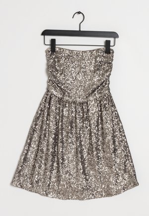 Zilveren sequin jurk zonder bandjes, hangend aan een zwarte hanger tegen een witte achtergrond, met geplooide taille en een uitlopende rok.