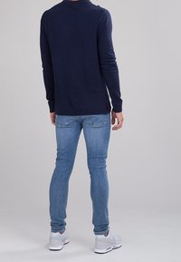 Granatowy sweter z długimi rękawami, połączony z jasnoniebieskimi obcisłymi dżinsami. Białe trampki z jasnoszarymi akcentami. Widoczna miękka faktura.