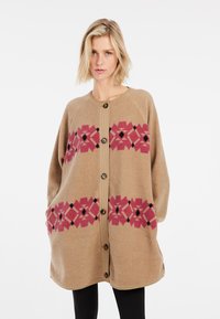 Beige fleecedeken met een bloempatroon in roze en zwart, voorzien van een knoopsluiting aan de voorkant en een comfortabele pasvorm. Zachte textuur en lange mouwen.