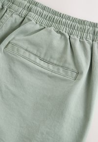 Shorts en coton vert clair avec une finition texturée, dotés d'une ceinture élastique et d'une poche arrière avec une ouverture rectangulaire.