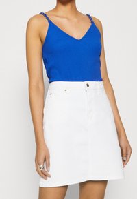 Modrý žebrovaný tílko s výstřihem do V a ozdobnými ramínky, doplněné bílou džínovou minisukní s předním zapínáním na knoflíky a kapsami.