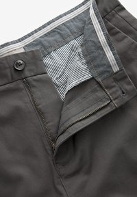 Dunkelgraue Hose mit einem Reißverschluss- und Knopfverschluss, gestreiftem Innenbund und kontrastierenden Nähten entlang der Kanten.