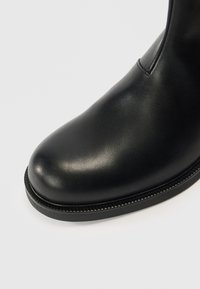 Juodi odiniai kulkšnies batai su apvalia nosimi, lygiu paviršiumi ir subtiliais siuvimo detalėmis šone ir aplink pado kraštą.