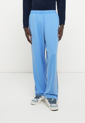 Pantalones de chándal de forro polar azul claro con cintura elástica, tiras laterales y un corte relajado, combinados con zapatillas blancas y azules.