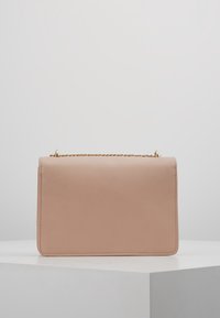 Clutch rettangolare in pelle nuda con una tracolla a catena dorata, esposta chiusa su un piedistallo geometrico bianco contro uno sfondo grigio chiaro.