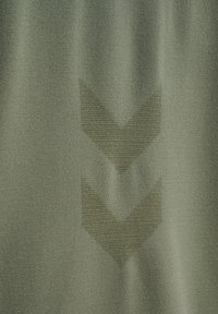 Zielony materiał tekstylny z fakturowanym wzorem obejmującym dwa szewrony skierowane w dół. Tkanina wydaje się miękka i ma gładkie wykończenie.