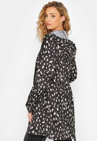 Czarna wodoodporna kurtka z białym kropek wzorem, z elastycznym ściągaczem w kapturze i w talii, długimi rękawami oraz nieco dłuższym tyłem.