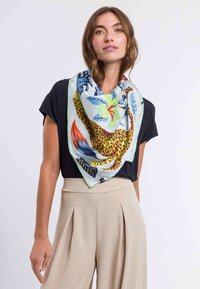 Foulard quadrato in seta con stampa leopardata e motivi floreali colorati, bordato da un bordo verde, indossato sopra una maglietta nera.