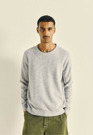 Jasnoszary sweter z okrągłym dekoltem, wykonany z miękkiego materiału, z prążkowanymi mankietami i dołem, w połączeniu z oliwkowymi spodniami. Minimalistyczny design.