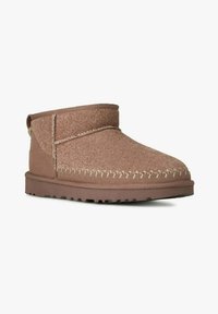 Stivali alla caviglia in suede marrone con punta arrotondata, tomaia testurizzata, cuciture a vista e suola piatta in gomma. Include un'etichetta posteriore per la facilità di indossarli.