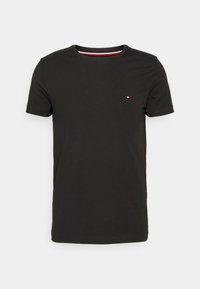 T-shirt in cotone nero con collo rotondo e maniche corte, caratterizzato da un piccolo logo rosso, bianco e blu sul petto e una finitura interna del collo in contrasto.