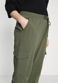 Pantaloni jogger verde oliva realizzati in tessuto morbido, con vita elastica, cordoncino e tasche laterali con dettagli a patta.