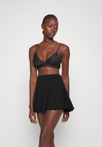 Zwarte bralette met dunne bandjes, gecombineerd met een zwarte flared rok. Beide kledingstukken hebben een gladde textuur en een fitted, modern ontwerp.