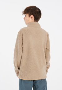 Sudadera de forro polar beis con cuello alto, exterior texturizado y hombros caídos. El dobladillo es ligeramente más largo en la parte de atrás.