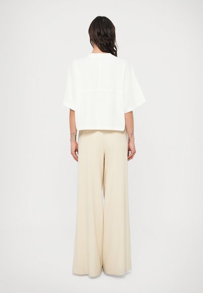Λευκό, κοντό τοπ με ανοιχτά μανίκια· μπεζ παντελόνι με φαρδιά μπατζάκια, λεία υφή και αέρινο σχέδιο· μινιμαλιστικό στυλ, χωρίς διακοσμητικά στοιχεία.