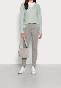 Pull vert clair en maille avec col en V, pantalon gris slim, baskets blanches et un sac à main gris doux avec une bandoulière froncée.