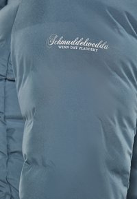 Sötétkék pufferszerű kabát sima textúrával, steppelt mintázattal. Fehér hímzett logo található a mellek részen.