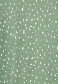 Tecido verde com um padrão de pontos brancos dispersos. Textura suave, material de peso médio. O design apresenta pontos de formas irregulares em tamanhos variados.