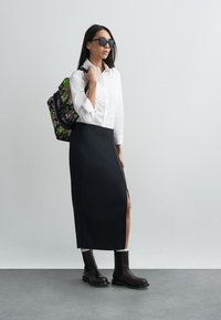 Μαύρη midi φούστα με φερμουάρ στο πλάι, λευκό πουκάμισο με κουμπιά, σκούρα γυαλιά ηλίου και καφέ μποτάκια αστραγάλου. Σακίδιο με λουλουδάτο μοτίβο στον έναν ώμο.