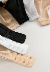 Trois soutiens-gorge en noir, blanc et beige avec des fermetures à agrafes disposés sur une surface claire.
