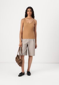 Top ajustado sin mangas de color claro combinado con pantalones cortos grises claros. Zapatos negros de punta abierta y un bolso marrón texturizado completan el conjunto.
