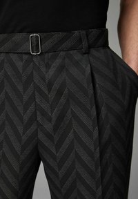 Pantalons noirs à motifs présentant un design en chevron, taille plate avec un détail de boucle en argent, poches latérales et tissu texturé.