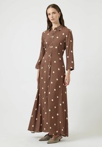 Brązowa sukienka zapinana na guziki z długimi rękawami, ozdobiona dużymi kremowymi groszkami i luźnym fasonem. Do tego dobrane baleriny w neutralnym kolorze.