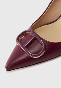 Burgundi odinė batai su smailiu nosimi, papuošti violetiniu ir auksiniu sagtimi, su lygiu paviršiumi ir elegantiška siluetu.