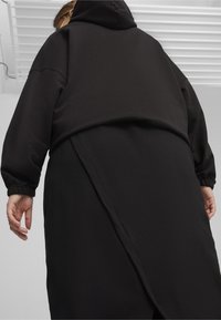 Svart hoodie med lös passform, ribbat tyg och elastiska ärmslut. Har en längre bakre fåll och detaljerad söm.