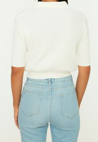 Weißes kurzärmeliges Oberteil mit Rippstruktur und Kragen, kombiniert mit hellblauen, hoch taillierten Jeans mit zwei Gesäßtaschen.