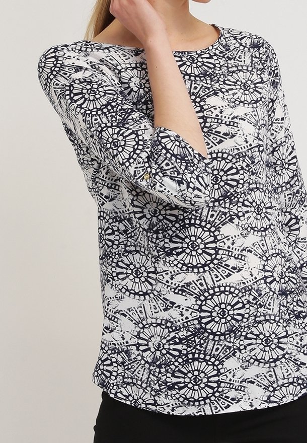 Bílá blůza s námořnickým kruhovým vzorem, kulatým výstřihem a tříčtvrtečními rukávy, vyrobená z hladké látky s jemným leskem.