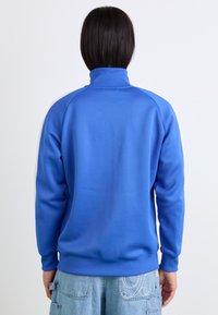 Pulover albastru cu guler înalt, margini ribetate și mâneci lungi. Fabricat dintr-un material neted, cu o culoare uniformă, fără modele sau accente vizibile.