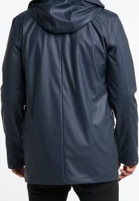 Mörkblå vattentät kappa i jämn, glänsande material. Har en huva, långa ärmar och knapplösningar vid ärmsluten.