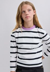 Camisa de manga larga a rayas en blanco con líneas horizontales negras, con un cuello de canalé lavanda y un pequeño bolsillo en el lado izquierdo.
